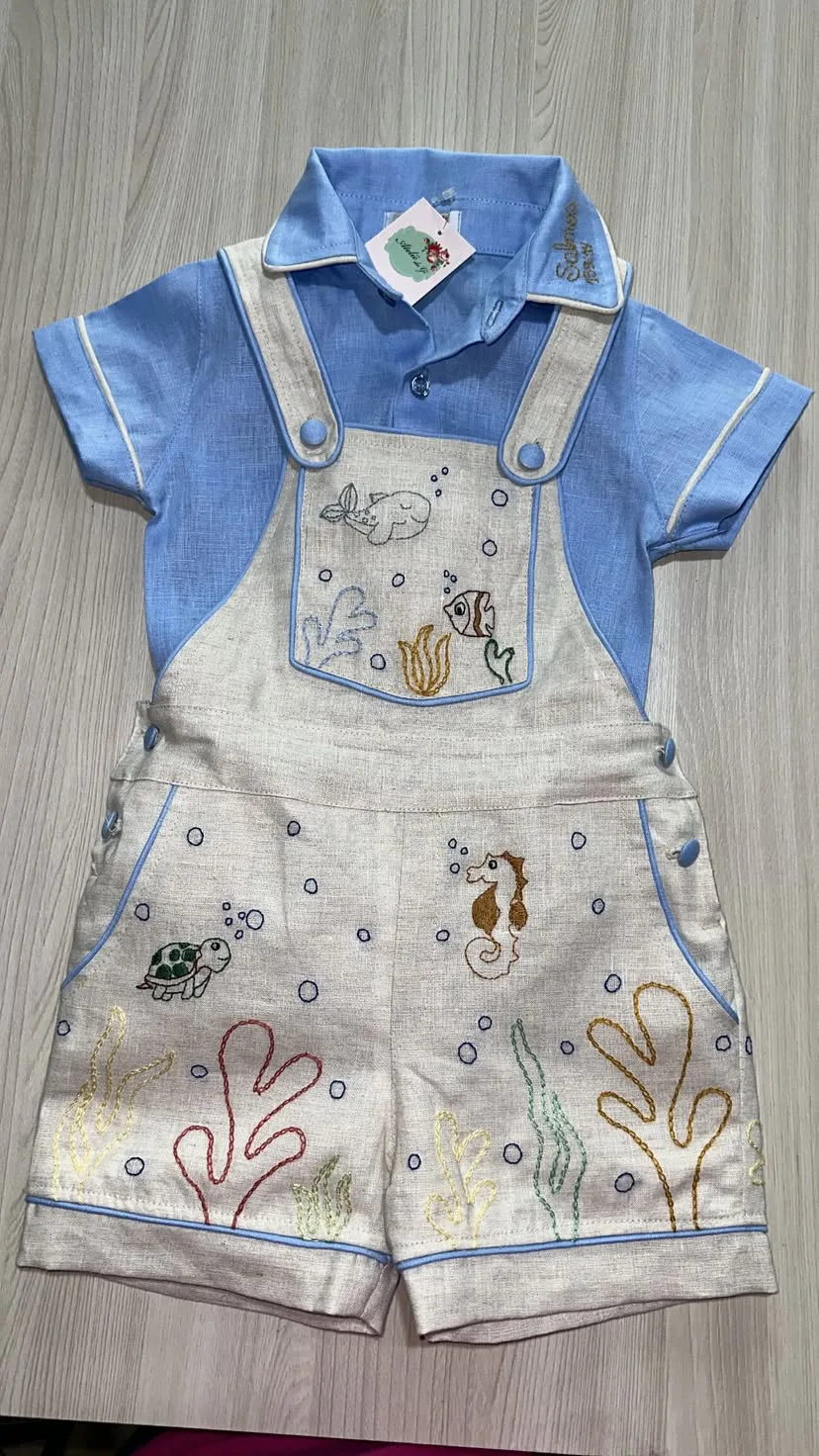 Jardineira Premium em linho natural com camisa combinando, bolsos frontais com aba funcional, fivela artesanal nas alças e pesponto duplo em linha contrastante